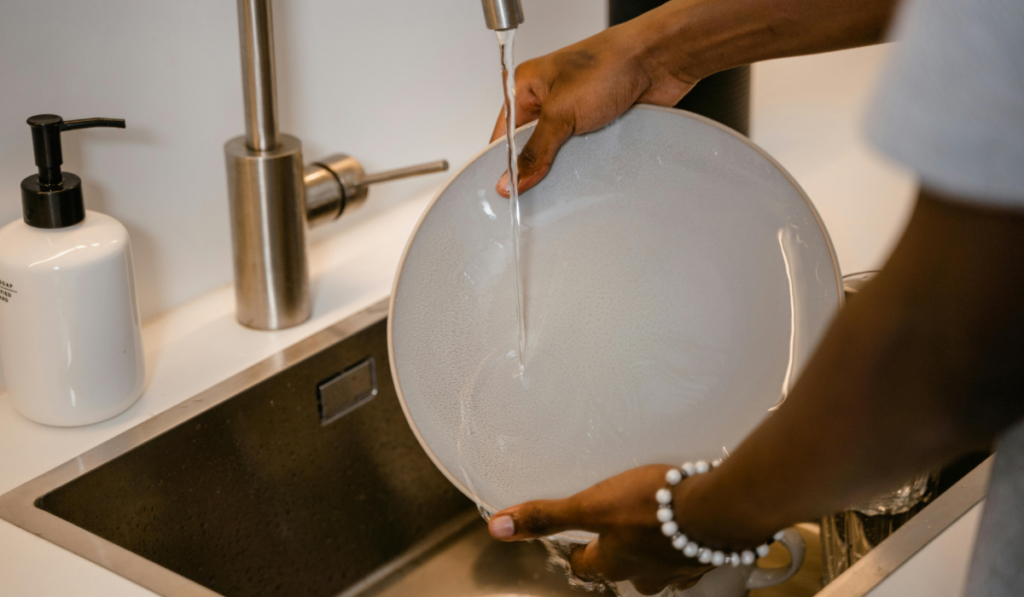 Person washing a plate under running water in a modern kitchen.